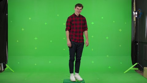 A young man dancing spinning in circle on green screen background. Attractive guy making content for social media. Modern blogger creating a master class. Chroma key