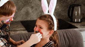 Slow motion. A boy in Easter bunny ears paints a girl's face with paint. The girl laughs