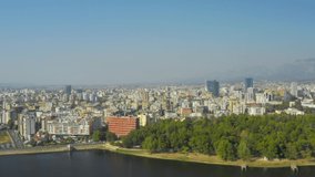 A drone view of the skyline of Tirana, Albania. Park on the Artificial Lake, Grand Park of Tirana, mountains, skyscrapers, city, aerial, downtown, park - 4K Drone Video Footage