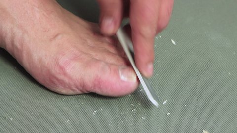 A man's hand files the nail of the big toe with a file. We do the pedicure ourselves. Self care for feet, concept. Isolated video, close-up. Warm, soft light. UHD 4K.