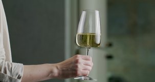 glass of white wine in a woman's hand. White wine splashing in a glass from side to side like waves. Glass with splashing wine