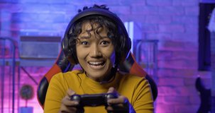 Young woman gamer playing online video game at home. She playing online games with neon lights background.