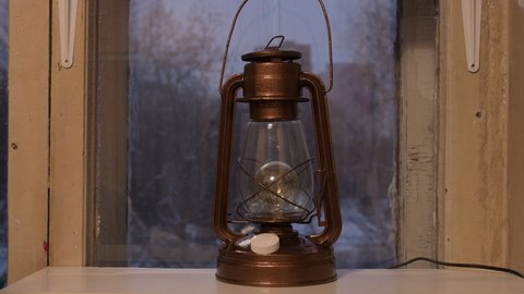 An old oil lamp has been converted into a modern electric lamp with a dimmer. A kerosene lamp is on the window. The concept of reasonable consumption