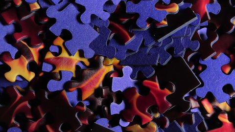 Background of Colored Puzzle Pieces that Slowly Rotating Counterclockwise - Top View, Close-Up. Texture of Incomplete Red and Blue Jigsaw Puzzle with Low Key Light - Right Rotation