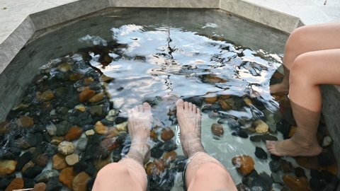 Couple tourist sitting and soaking foot in natural mineral water of hot spring basin at resort. Vacation and holiday concept