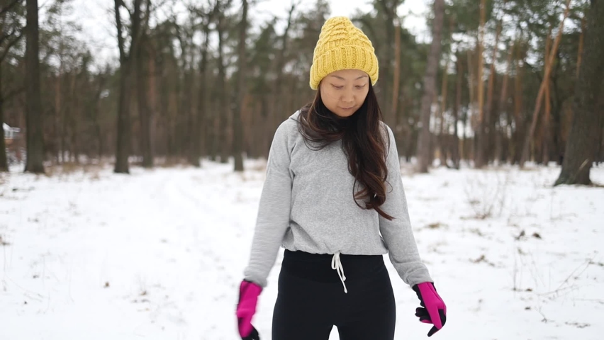 Beautiful young asian woman preparing for training. Snowy forest morning fitness.