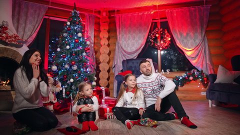 KYIV, UKRAINE - August 2021: Cheerful family sitting near a fireplace and meeting Santa with a big bag. Kids rejoicing when seeing presents. Santa comes to the family 