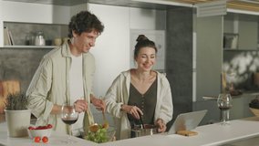Positive married couple watching funny videos on digital tablet while cooking together on kitchen. Husband and wife enjoying common time at home. - Powered by Shutterstock - Get 15% off with code: PIKWIZARD15