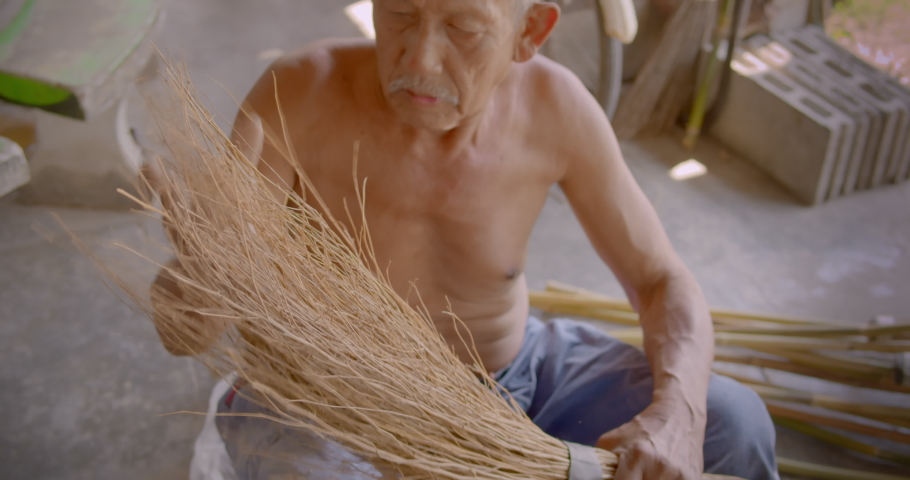 Asian male farmer who is an elderly person makes brooms from the grass that has many names called Paddy's lucerne, Queensland hemp , Arrowleaf sida , Common sida , Cuba juite for extra income. Royalty-Free Stock Footage #1086780377