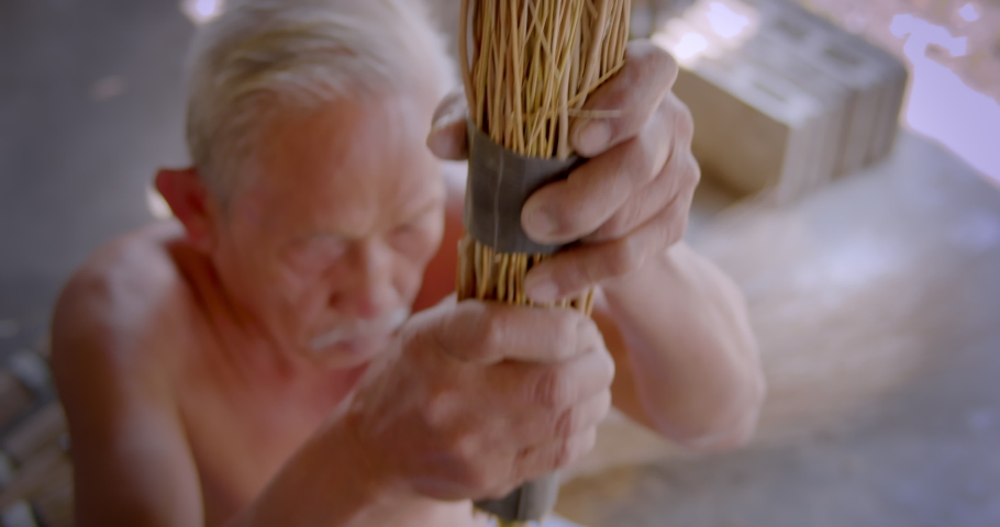 Asian male farmer who is an elderly person makes brooms from the grass that has many names called Paddy's lucerne, Queensland hemp , Arrowleaf sida , Common sida , Cuba juite for extra income. Royalty-Free Stock Footage #1086780380