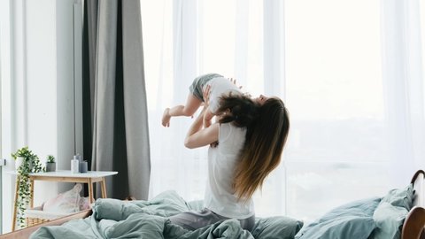 Family morning leisure together in sunny apartment in the bed. Mother playing with little beautiful daughter in the bedroom throwing her up.