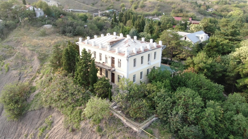 A twostorey building surrounded by green trees at the top of a hill. Aerial view