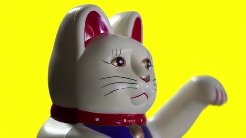 A Maneki-neko, also known as a Lucky Cat, or Happy Cat, Figurine on Yellow Background. Close Up. 4K Resolution.