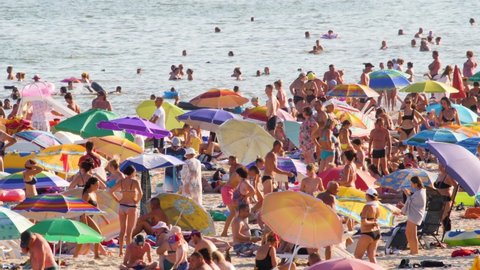 Odessa, UKRAINE - August 10, 2021: The Black Sea summer beach crowded people vacation sea travel. Lots people on the beach full travelers. Many people relaxing on the beach shore crowd sea slow motion