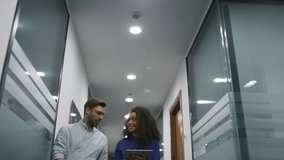 Multhiethnic business couple talking financial project using tablet computer in office corridor. Two entrepreneurs discussing corporate data. Employees walking together. Meeting communication concept. - Powered by Shutterstock - Get 15% off with code: PIKWIZARD15