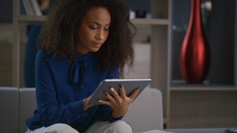 Calm african american entrepreneur woman working tablet drinking coffee in home office. Young business lady using touchpad digital tab in workplace. Boss girl browsing internet. Remote work concept.