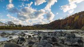 Mountain river wild stone bank with rapids against colorful trees growing on hill slopes under blue sky, floating clouds in autumn 8K video time-lapse