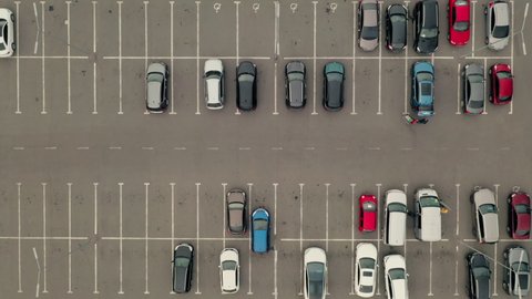 Blue car pulls out of the parking lot. Car leaves the parking lot - an aerial top overhead view. Parking with many places near the supermarket - overhead view.