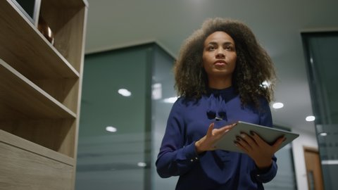 African american businesswoman working on go in office. Business woman ceo using tablet computer browsing internet in hallway. Focused manager walking corridor. Corporate professional busy concept. 