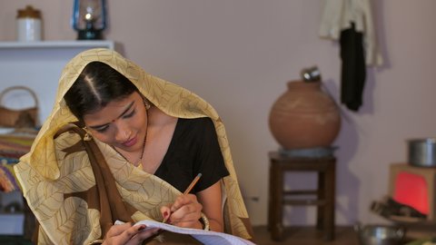 An attractive female farmer in a traditional Sari learning to write - Shiksha, Beti padao beti bachao, education . A rural married woman studying at home - an Indian village, a rural household
