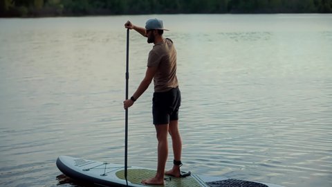 Man Stand Up Paddle Boarding. Warm Summer Beach Vacation Holiday. Travel Paddles Paddleboard. Sup Board Journey. Bearded Man Relaxing On Sup Surf Swimming. Watersport Floating On Surfboard At Sunset