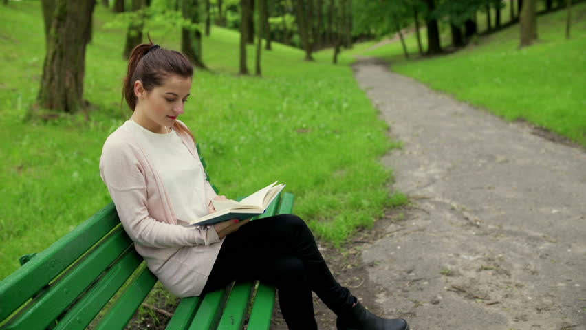 Woman sitting on the bench in the park and reading book
