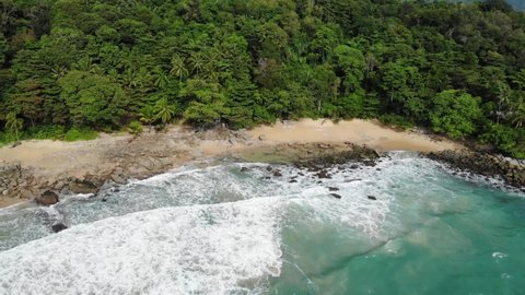 Turquoise Water Rocky Shore and Waves on a Wild Tropical Beach surrounded by Green Jungle and Trees