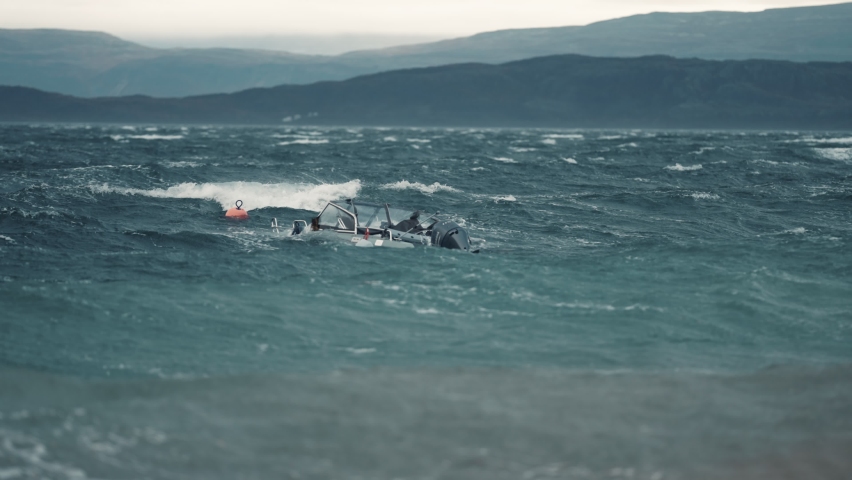 A small motorboat tied to a buoy is sinking, battling strong wind and powerful waves in the fjord.