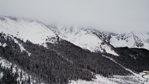 Loveland Pass Colorado USA. Drone Aerial Footage Of Rocky Mountains Alpine Mountain Slope Valley Covered in Dark Pine Trees and Low Clouds on Mountain Peaks.