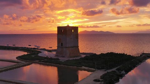 Aerial view over a tower at a salt production brine, sunset in Trapani, Sicily - rising, drone shot