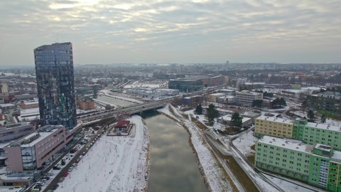 Snowy city of Olomouc, view of river with bridge and tall building with mirrored windows, cold winter panorama from drone