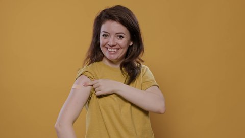 Portrait of smiling woman lifting sleeve and showing band aid after covid or flu vaccine for health care campaign in studio. Proud young person revealing bandage covering immunization spot.
