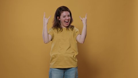 Rebel woman with positive attitude doing rock and roll hand gesture with tongue out wanting to party in studio. Happy smiling confident punk rocker person celebrating feeling like a winner.