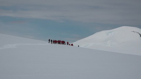 Antarctica Peninsula. A group of people hiking through the snow-capped hills of Antarctica. Scientist research group travel in Antarctica in sunny day. People hikers climbing mountain.