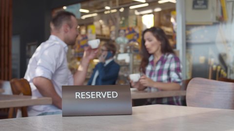 Waitress put reservation sign on table in cafe. Couple drink coffee on blurred background. Realtime. 
