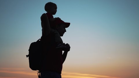 Happy family. Son sitting on neck of the father. Family silhouette in the park. Son plays with his father in the park on vacation. Summer sunset in field. Family holiday concept. Father day in nature.