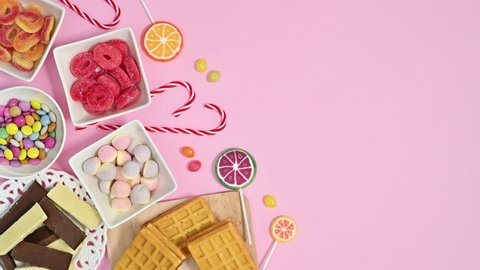 6k Bowls full with candies chocolates and lollypops appear on left side of pastel pink theme. Stop motion flat lay
