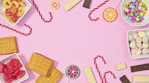 6k Candy frame for text made of moving gummy and chocolate candies and lollypops on pastel pink background. Stop motion animation flat lay