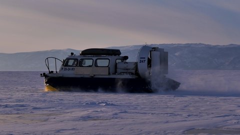 Khuzhir, Russia- March 1, 2021: Hovercraft driving at high speed on snow covered frozen ice surface of Lake Baikal at dusk. Slow motion shot.