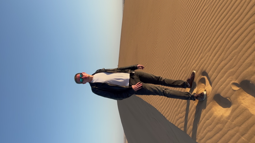Vertical video. Young man walks along sandy dunes. Dune 17 in Namibia. Summer vacations, wild desert nature in Africa at sunset.