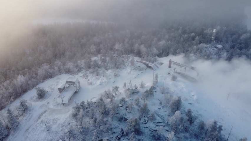 Drone footage of a flight over the hill of Vuokatinvaara, Kainuu, Finland., hiding in the dense fog at sunrise. View of snowy Finnish landscape from above. 4k Video.