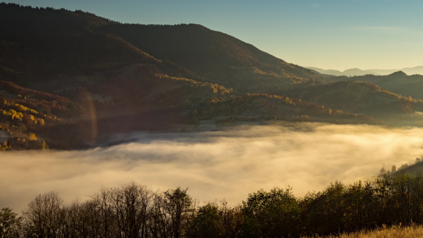 Sunset in highland with big forestry mountains and evening fog fills valley among hill slopes in autumn under orange sky 4K time-lapse video