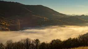 Sunset in highland with big forestry mountains and evening fog fills valley among hill slopes in autumn under orange sky 4K time-lapse video