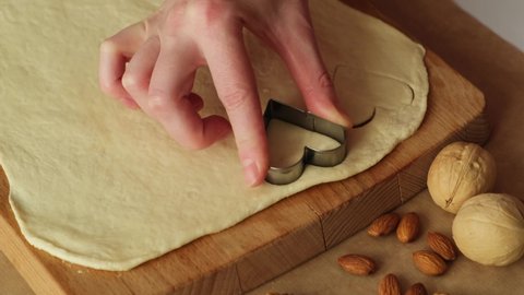 St Valentine's day concept. Homemade bakery. Women's hand cuts puff pastry, making heart shaped cookies on wooden cutting board. Close-up.