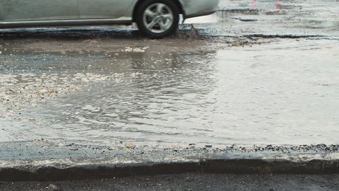 Deep potholes with water in bad weather, damaged road infrastructure. Cars drive slowly along the road with pits and puddles. Asphalt in violation of technology. Taxpayer money is wasted. UHD 4K.