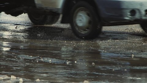 Dangerous pits on the asphalt, damaged road infrastructure after rain. Cars drive slowly along the road with potholes and puddles. Asphalt in violation of technology. Taxpayer money is wasted. UHD 4K.