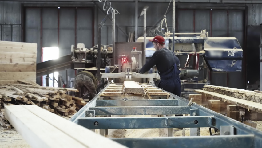 Two Male Workers Operating Industrial Saw. Industrial Saw In A Wood Production Process At Modern Timber Workshop. Industrial Saw Machine Used By Woodworkers To Cut Wooden Board Material