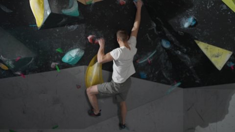 Slow motion, young climber training on a climbing wall, practicing rock-climbing and moving up.