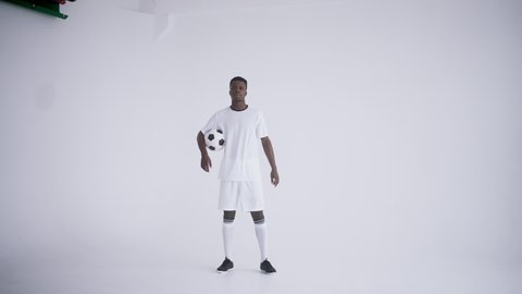 Portrait of an African ethnic footballer in a white uniform on a white background walking and looking at the camera the camera moves back from the headshot to the main plan