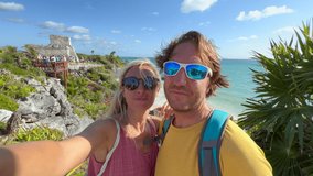 Happy couple taking selfie with Tulum ruins in Mexico. Two people, man and woman having fun on vacations and capturing video selfie while traveling. 